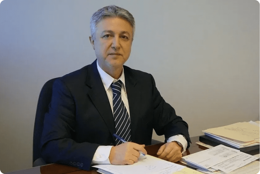 A man in a suit signing documents at a desk.