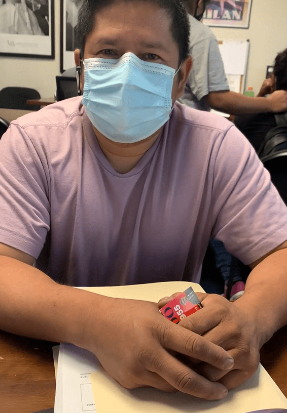 Person wearing a mask and pink shirt holding a snack.